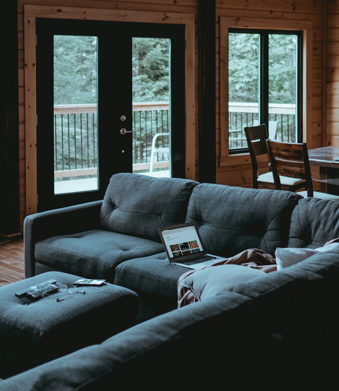 Gezellige woonkamer met een grijze bank en grote ramen met uitzicht op de natuur.